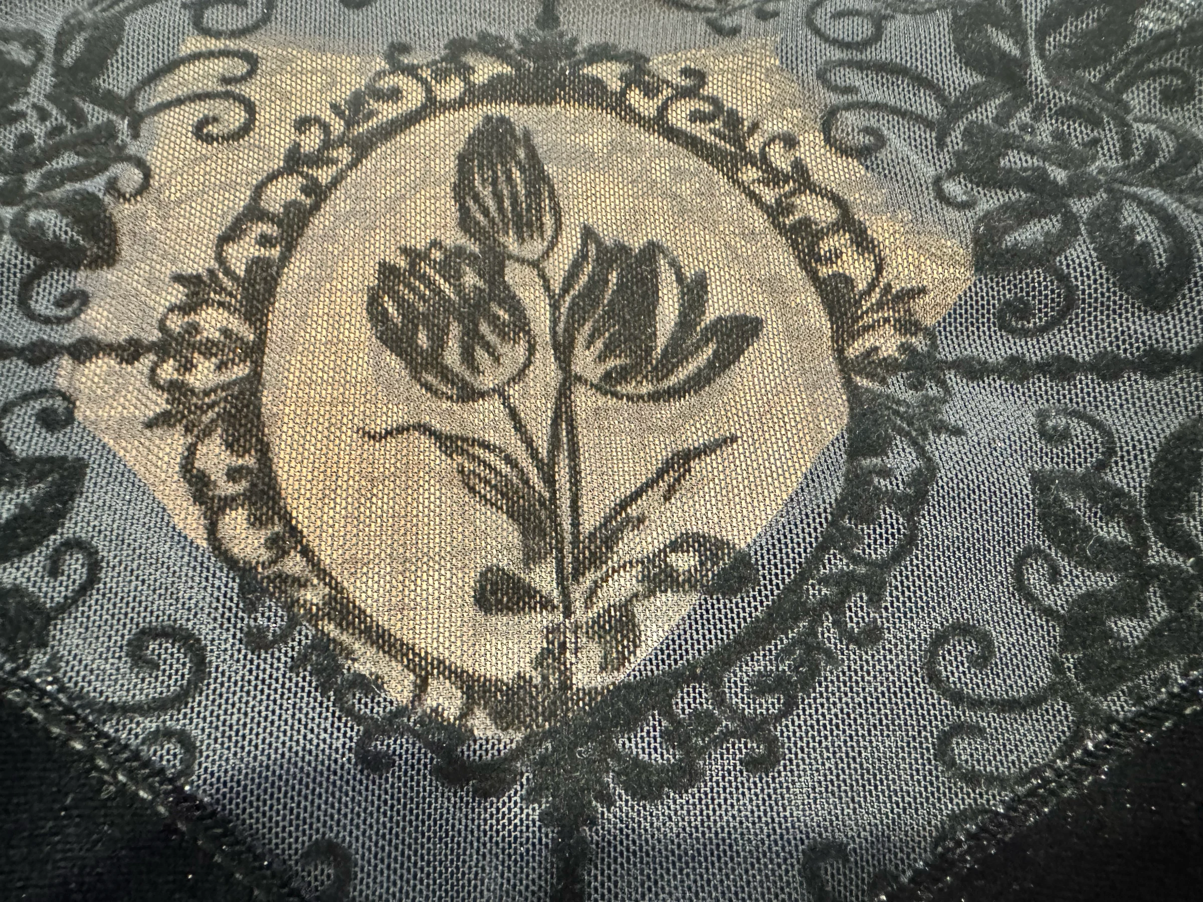 Close-up of black flocked floral and ornamental scrollwork patterns on sheer mesh fabric